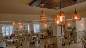 A spacious restaurant with multiple dining tables and chairs, hanging pendant lights, and a stone accent wall.