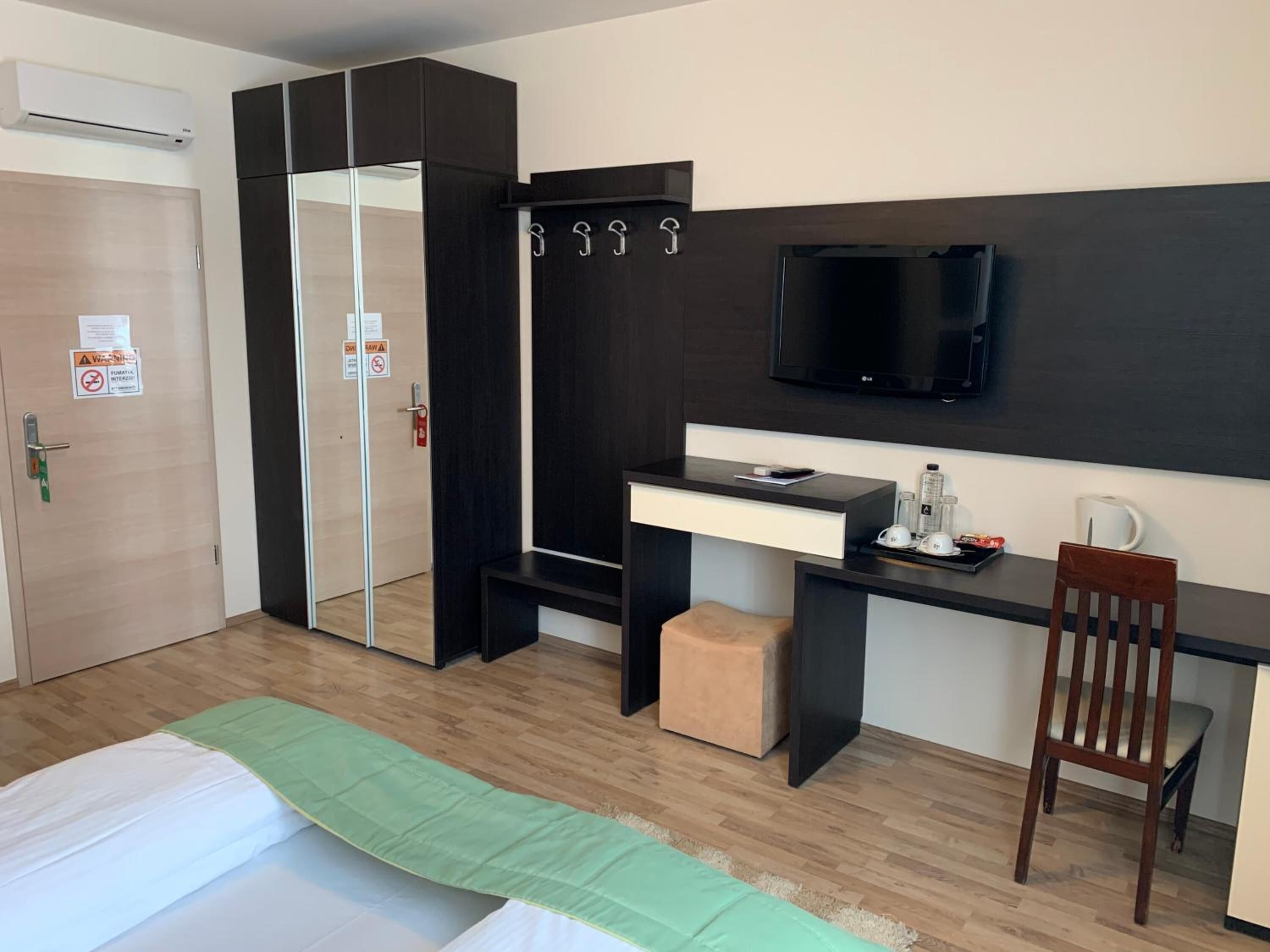 A hotel room with a bed, a desk with a TV, a chair, and a wardrobe.
