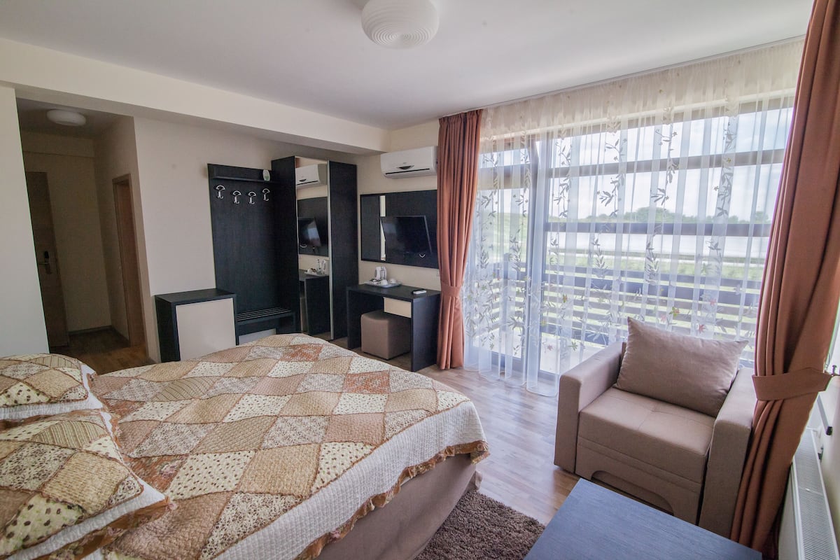 A hotel room with a bed, a desk, a chair, and a balcony with a view.