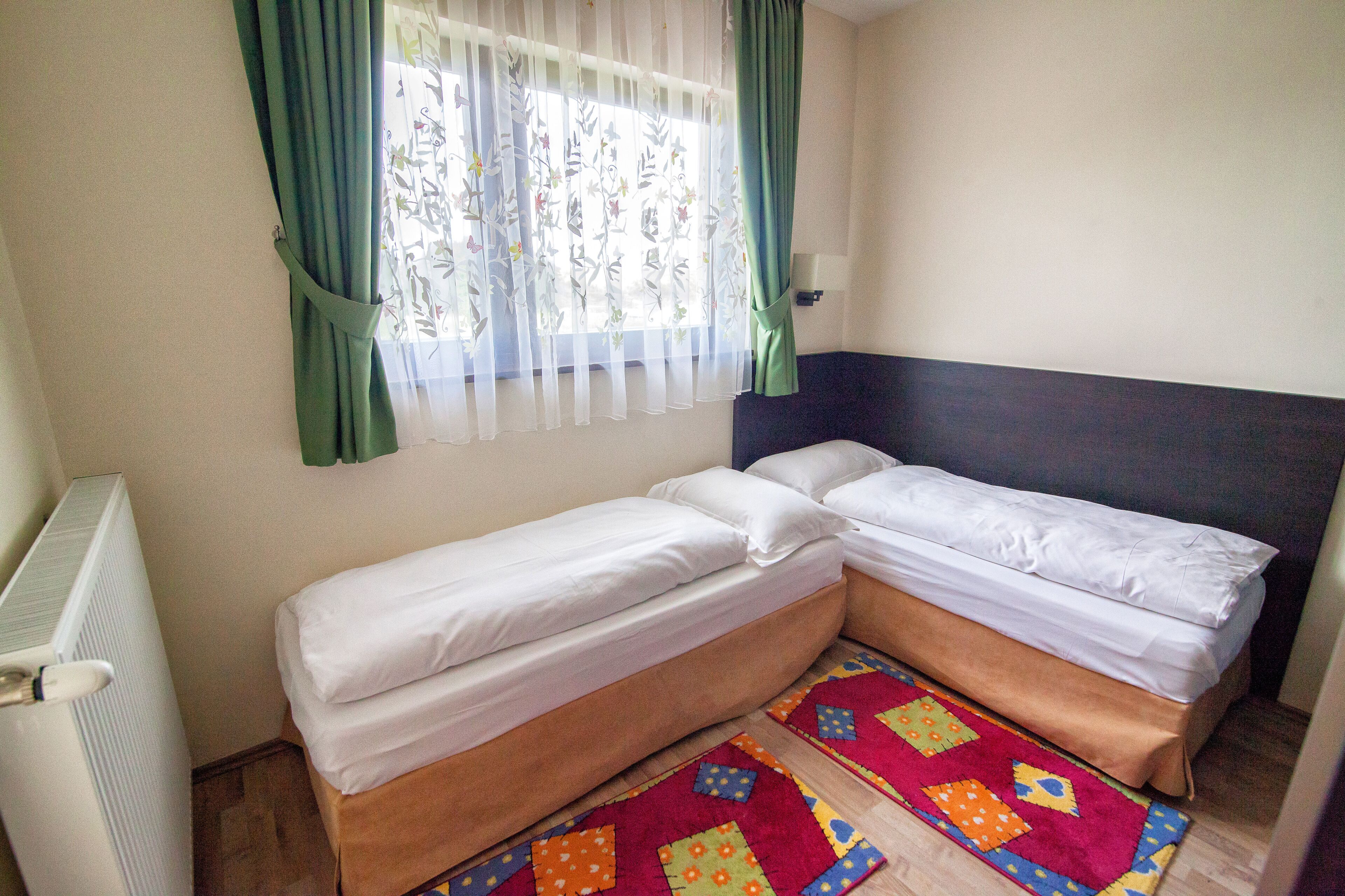 Pequeña habitación con dos camas individuales, un radiador y una alfombra colorida.