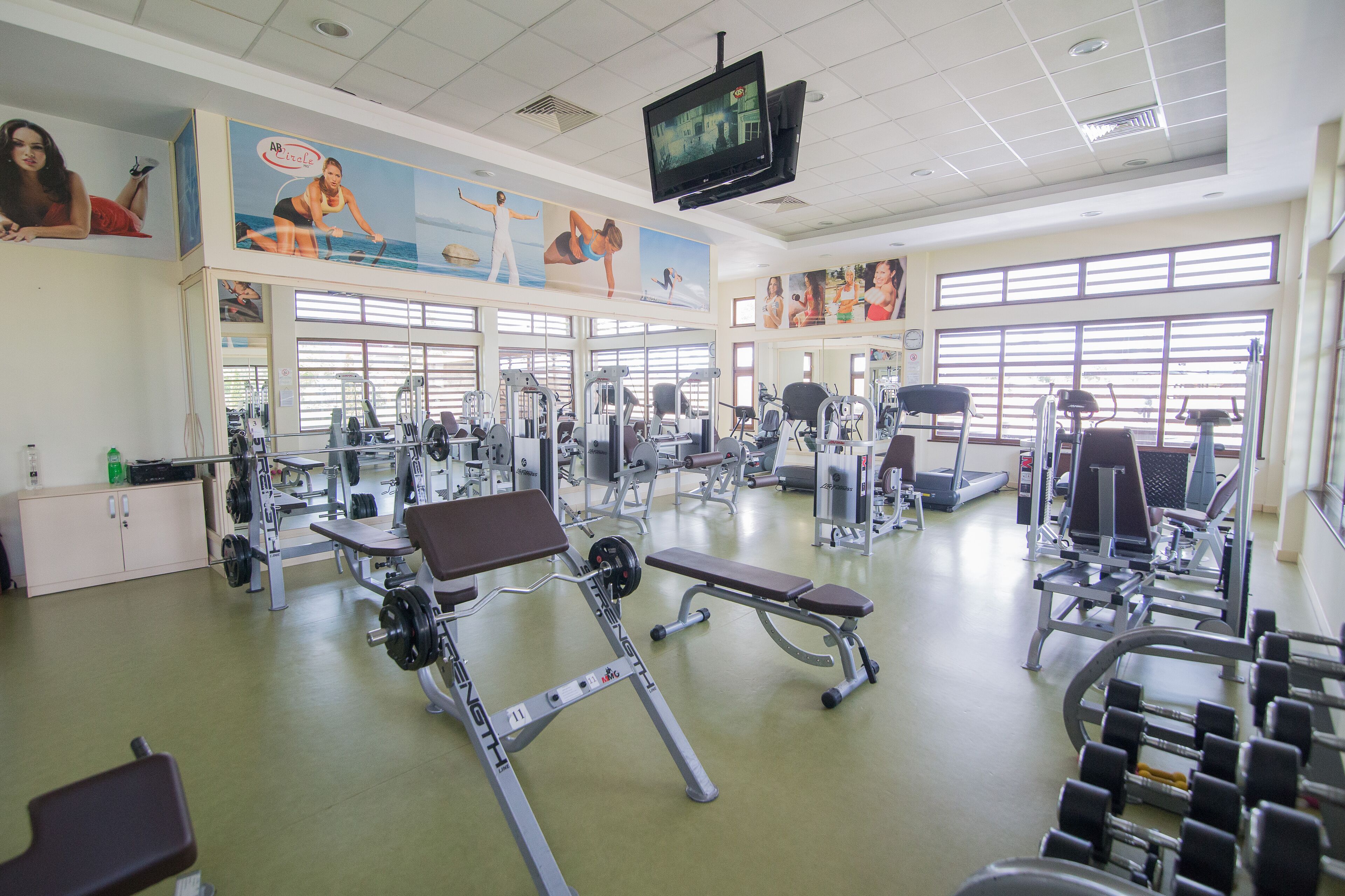 A gym with various exercise equipment, large windows, and motivational posters on the walls.