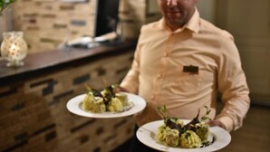 A person holding two plates of food in a restaurant with a brick wall background.