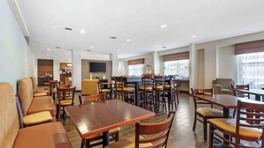 A spacious dining area with multiple wooden tables and chairs, a kitchen area in the background, and large windows providing natural light. - Sleep Inn & Suites Cumberland - LaVale (Cumberland)