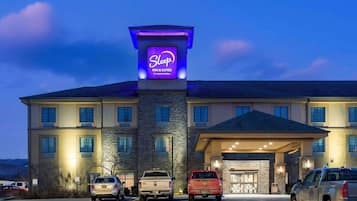 A Sleep Inn & Suites by Choice Hotels building with a stone facade, multiple windows, and a parking lot with several vehicles.