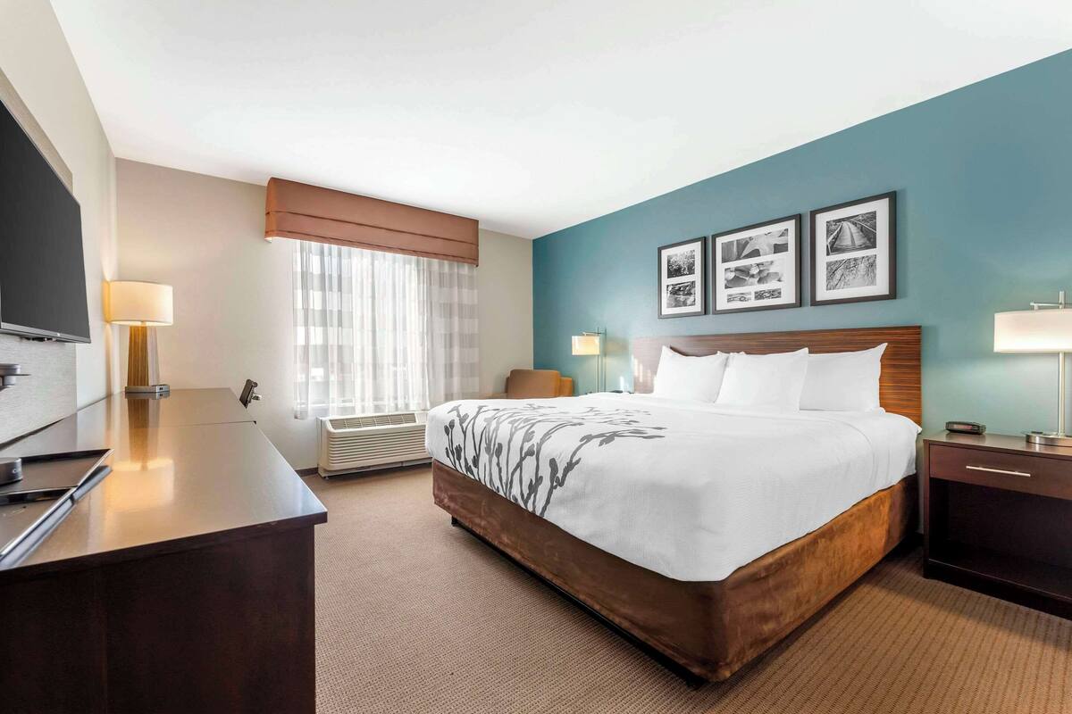 A hotel room with a bed, bedside table, lamp, and a flat-screen TV.