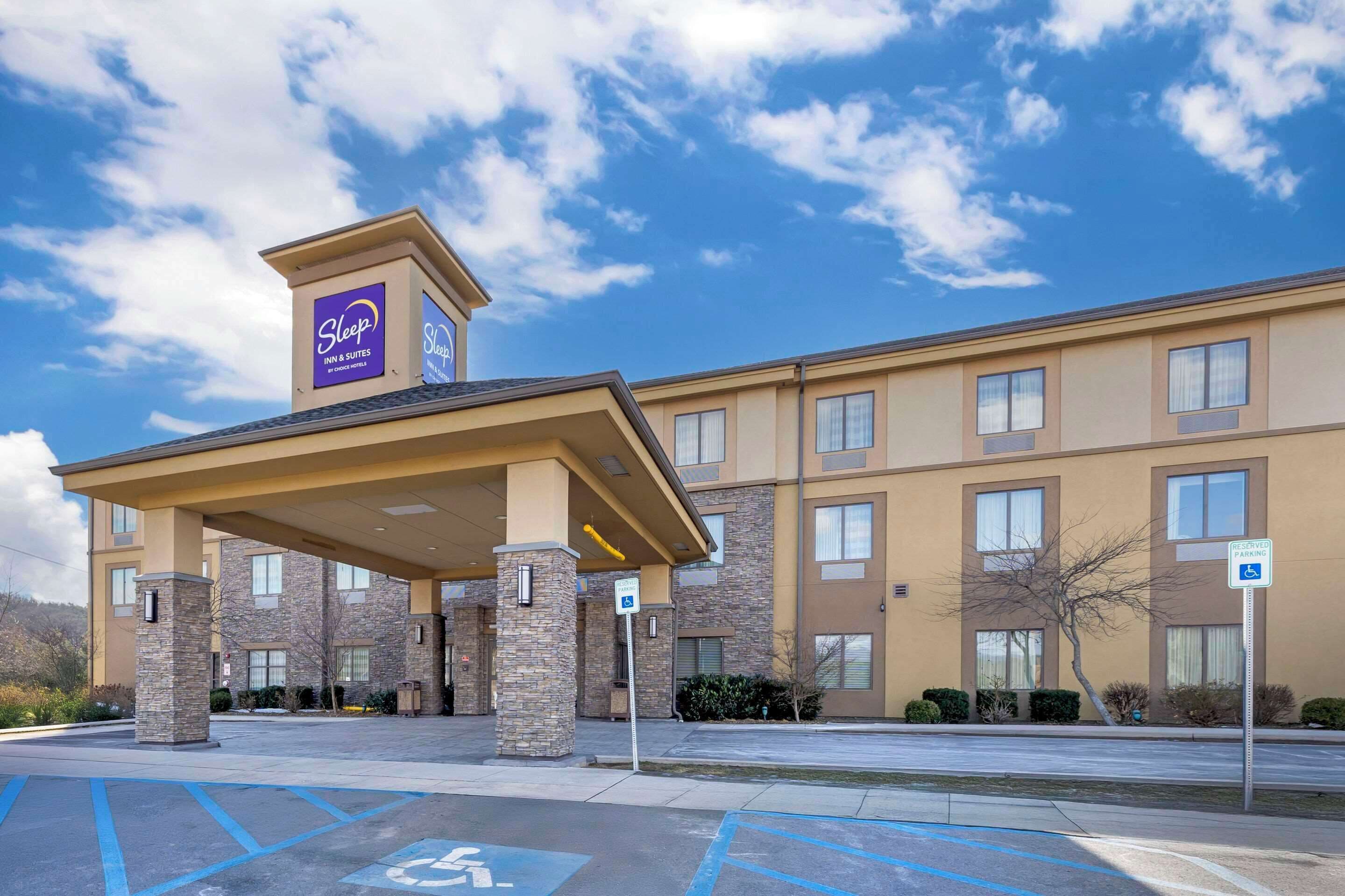 A Sleep Inn & Suites building with a covered entrance, stone pillars, and a parking lot with handicapped spaces.