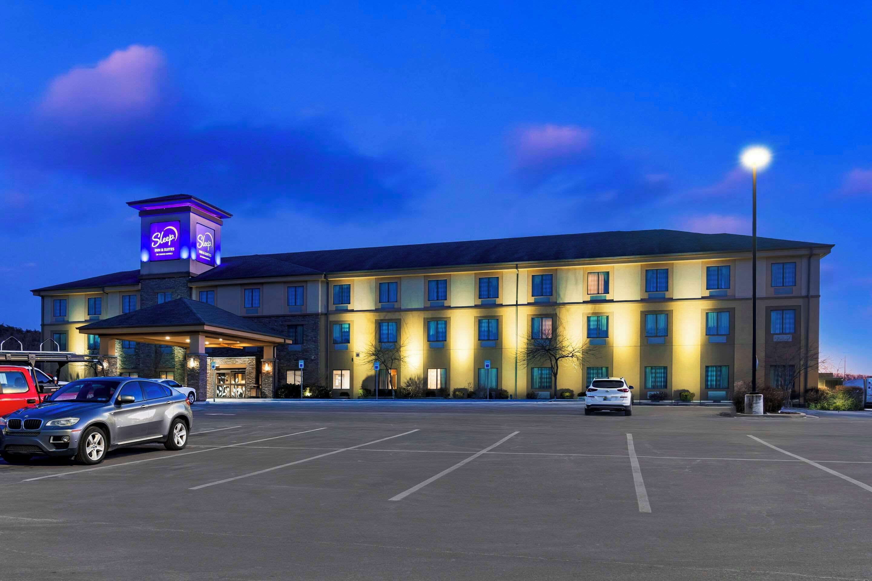 Un hotel con un amplio estacionamiento, un letrero de neón y varias ventanas.