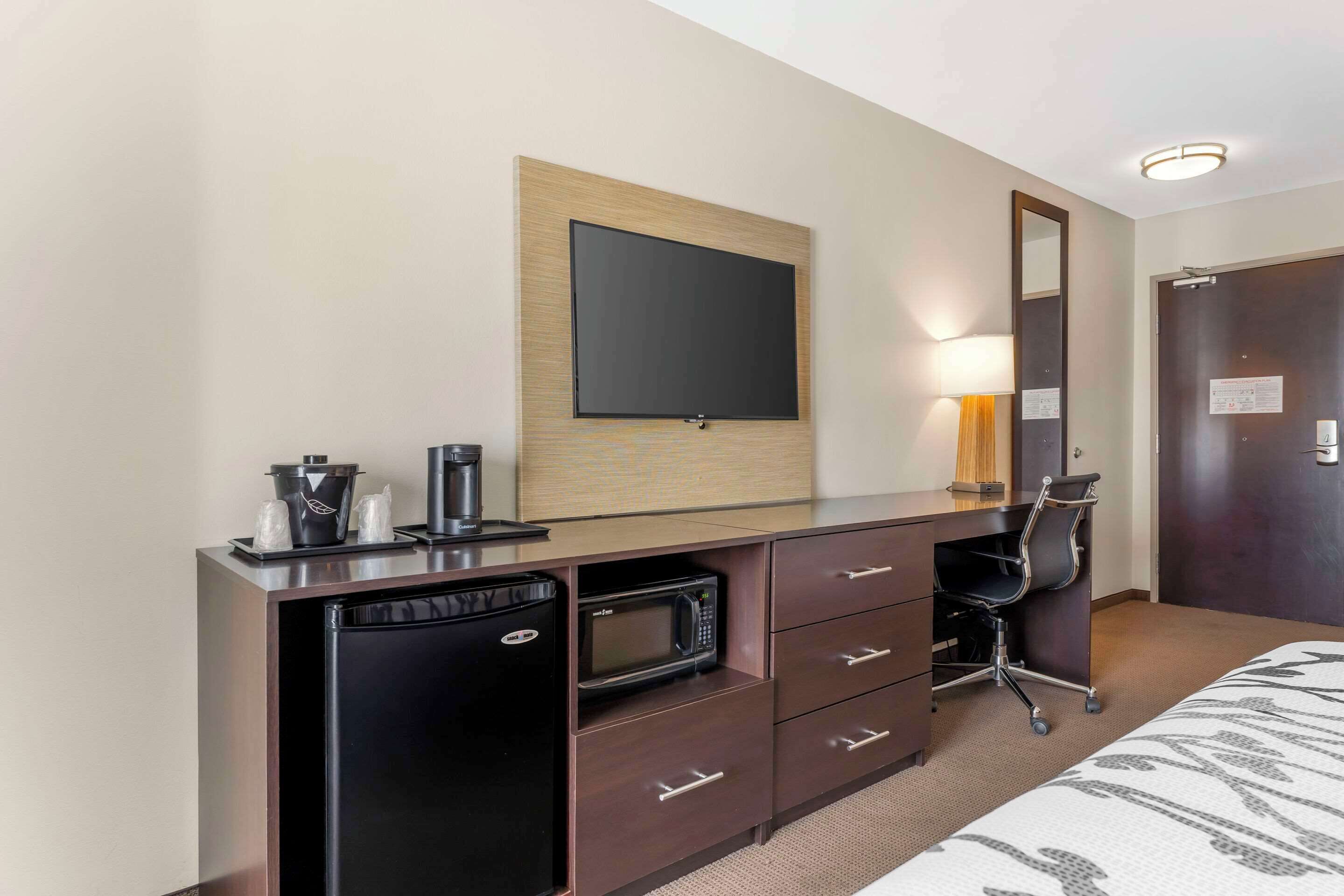 Une chambre d’hôtel comprenant un lit, un bureau avec un micro-ondes, un réfrigérateur, une chaise, un téléviseur fixé au mur et une porte avec une pancarte.