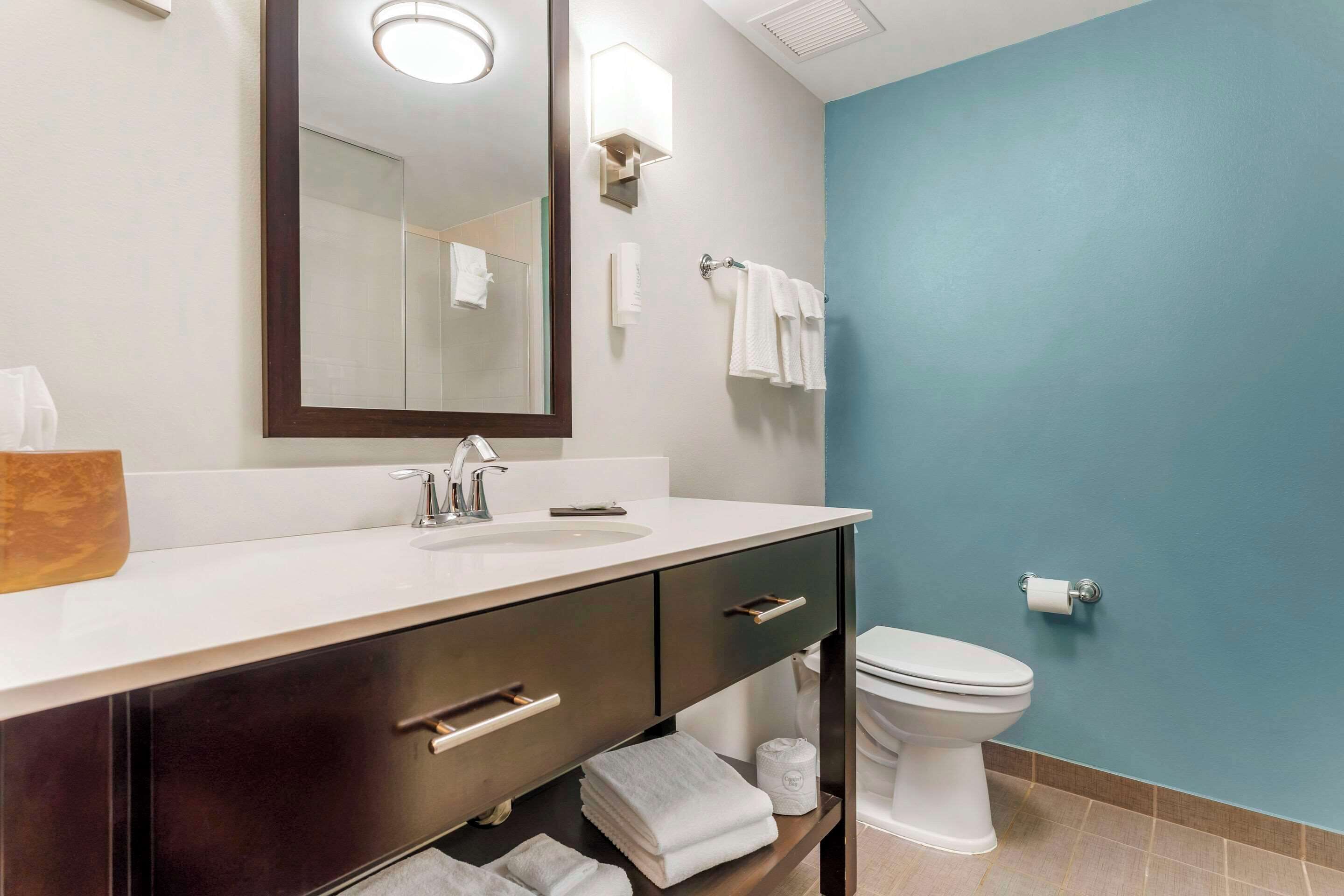 A bathroom with a white sink, dark cabinets, a mirror, a toilet, and a blue wall.
