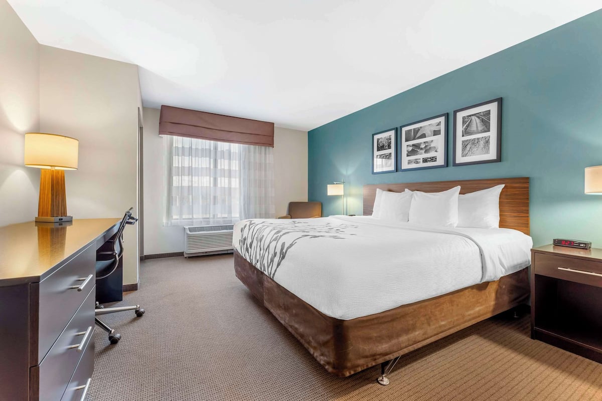 A hotel room with a bed, desk, chair, and a window with curtains.