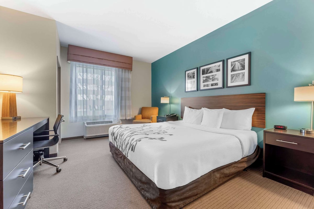 A hotel room with a bed, desk, chair, and a wall with three framed pictures.