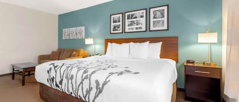 A hotel room with a large bed, a nightstand with a lamp, a chair, and artwork on the walls.