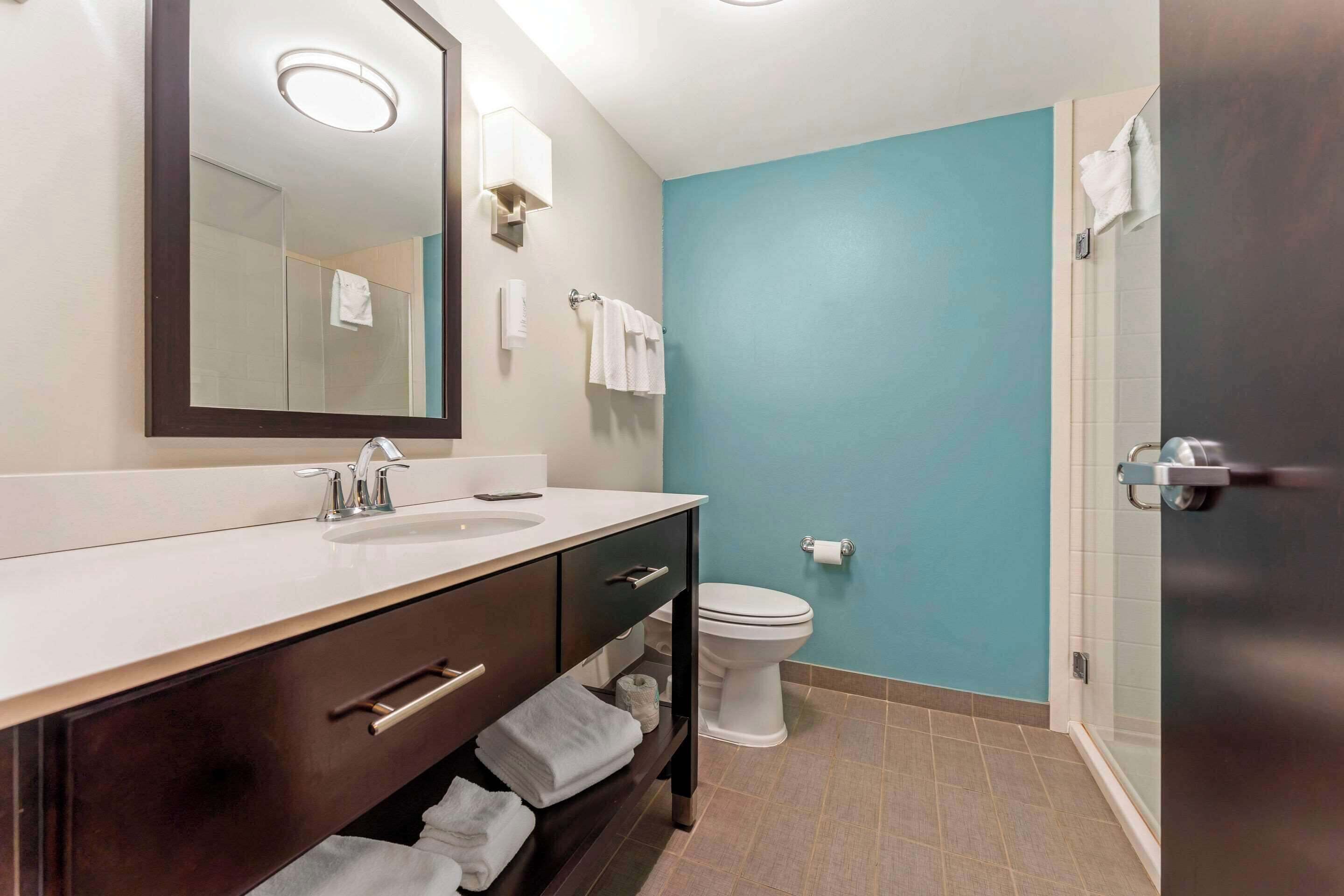 A bathroom with a white sink, dark wooden vanity, a mirror, a white toilet, and a blue wall.