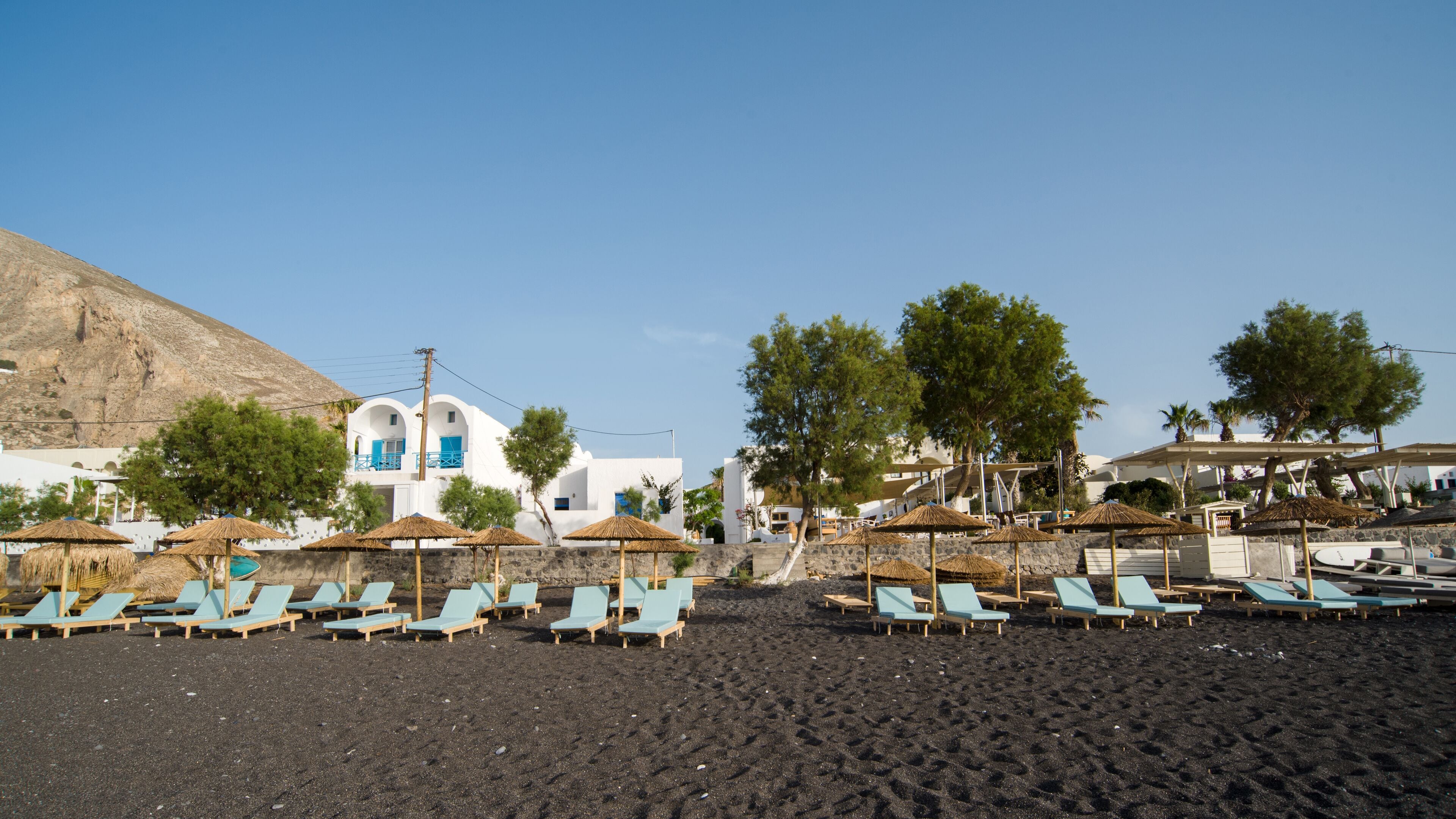 A beach with sun loungers, umbrellas, and a white building with blue accents.