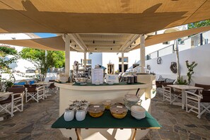 An outdoor breakfast setup with a buffet table, chairs, and umbrellas. - Santorini Crystal Blue (Santorini)