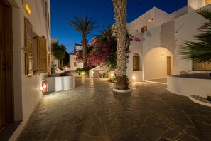 A stone-paved courtyard with white buildings, palm trees, and bougainvillea flowers. - Santorini Crystal Blue (Santorini)