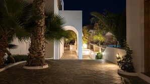 A stone-paved courtyard with palm trees, a white building, and a pool area. - Santorini Crystal Blue (Santorini)
