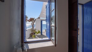 A room with a large window offering a view of the sea and a blue door. - Santorini Crystal Blue (Santorini)