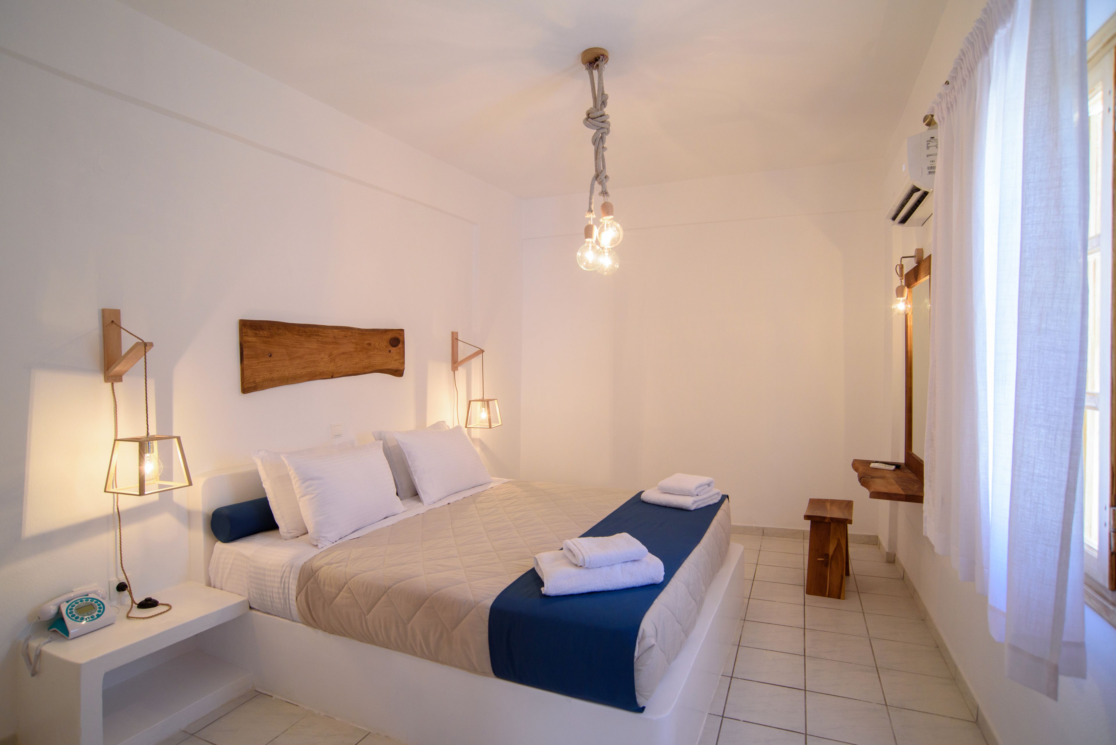 A neatly arranged bedroom with a bed, bedside tables, a hanging light fixture, and a window with curtains.