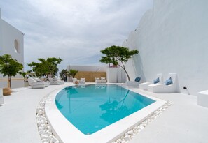 A pool area with white walls, a clear blue pool, and white lounge chairs. - Santorini Crystal Blue (Santorini)