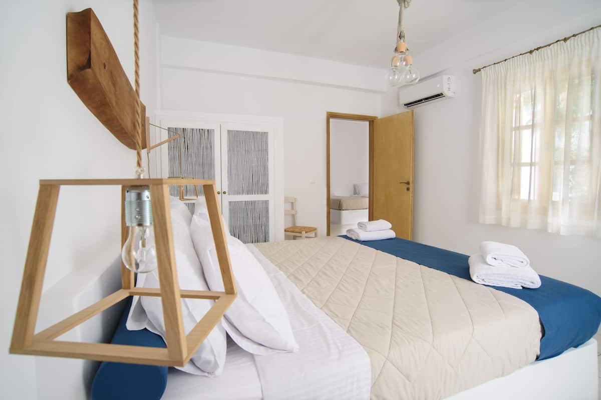 A bedroom with a bed, a hanging light fixture, a mirror, and a window with curtains.