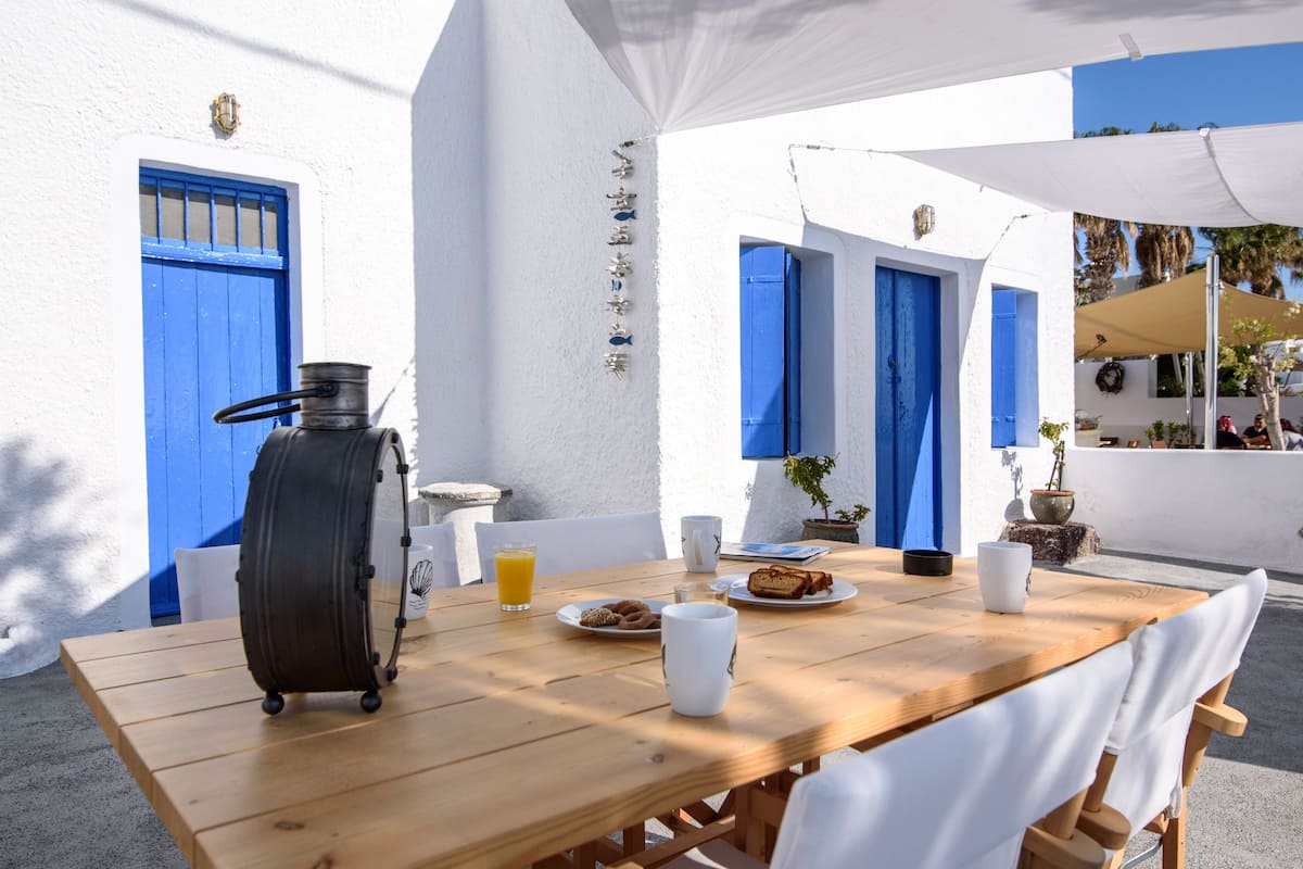 A wooden table with breakfast items, a kettle, and a blue door in a white-walled room.