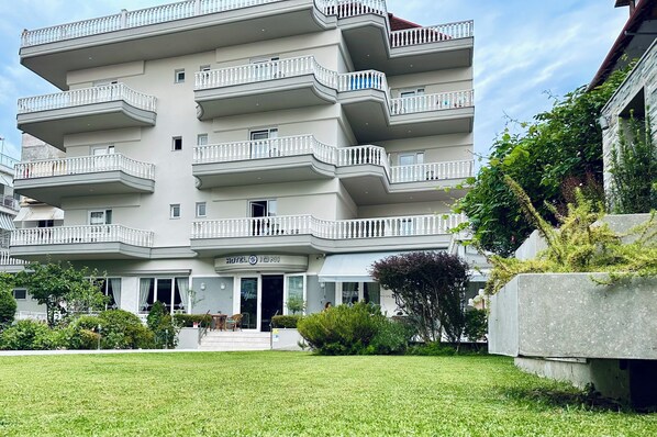 A multi-story hotel with balconies and a well-maintained lawn in front. - Hotel Ioni (Katerini)