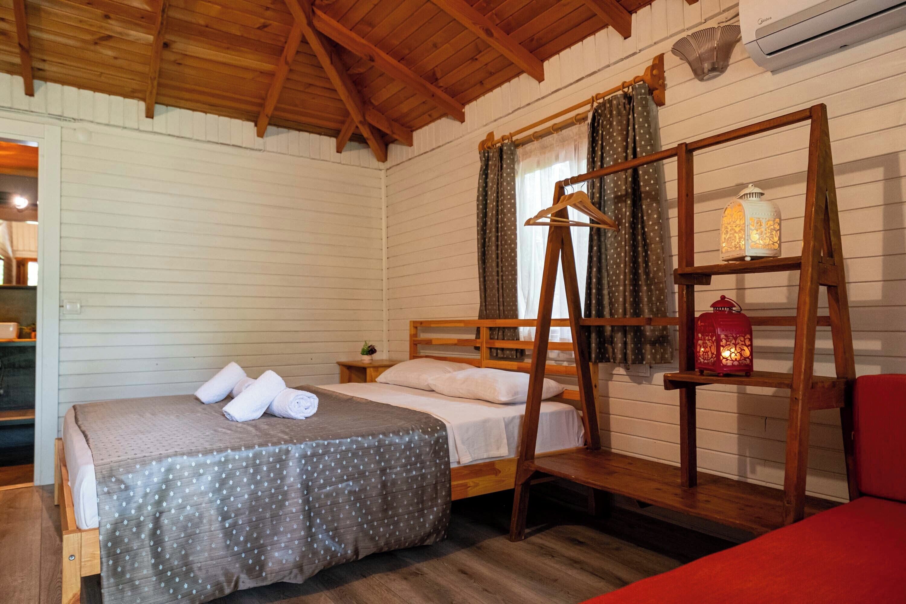 A wooden-framed bed with a polka dot bedspread, a wooden ladder, and a hanging light fixture.
