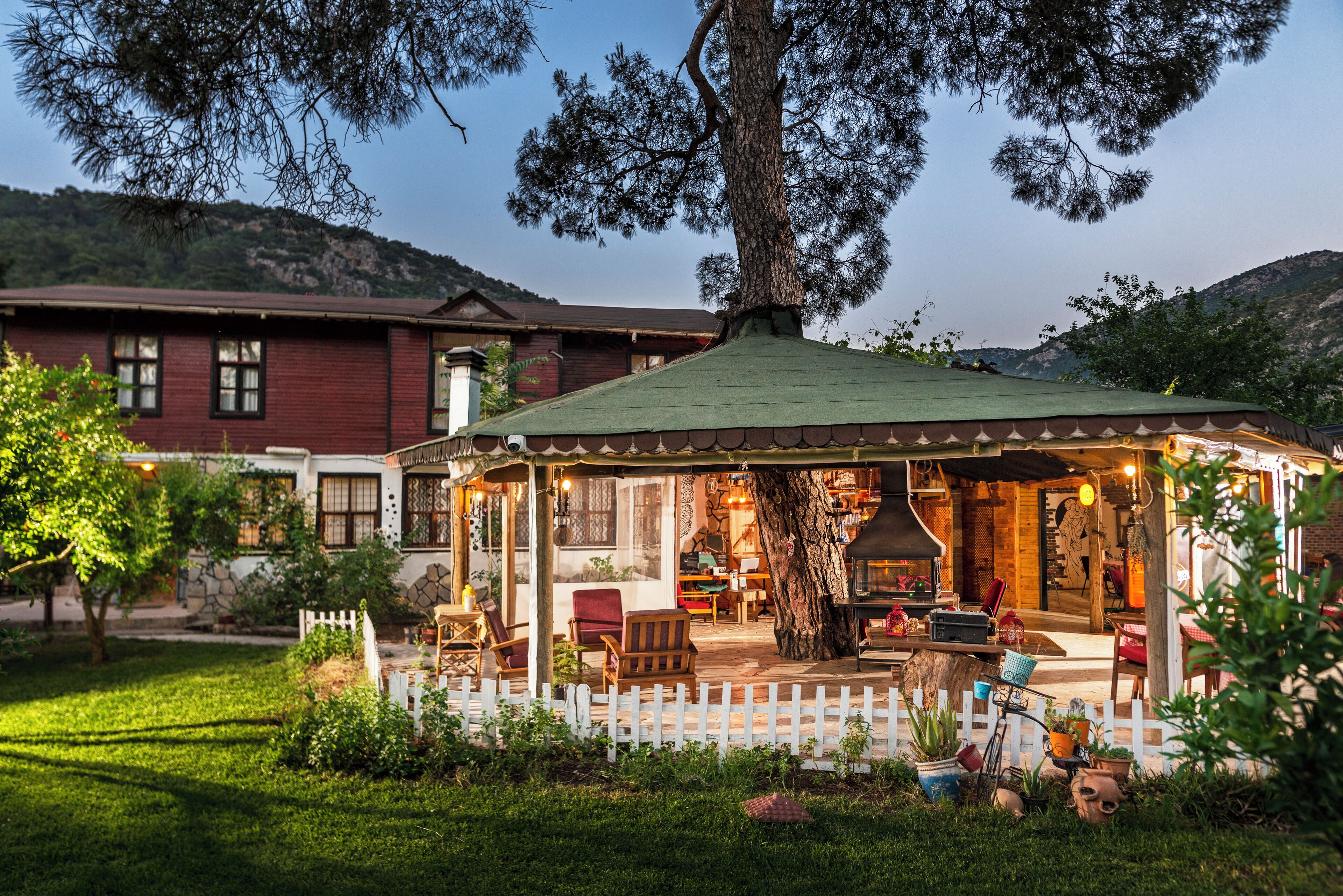 Un patio exterior acogedor con mesa y sillas de madera, rodeado por una cerca blanca de piquetes y un árbol grande que ofrece sombra.