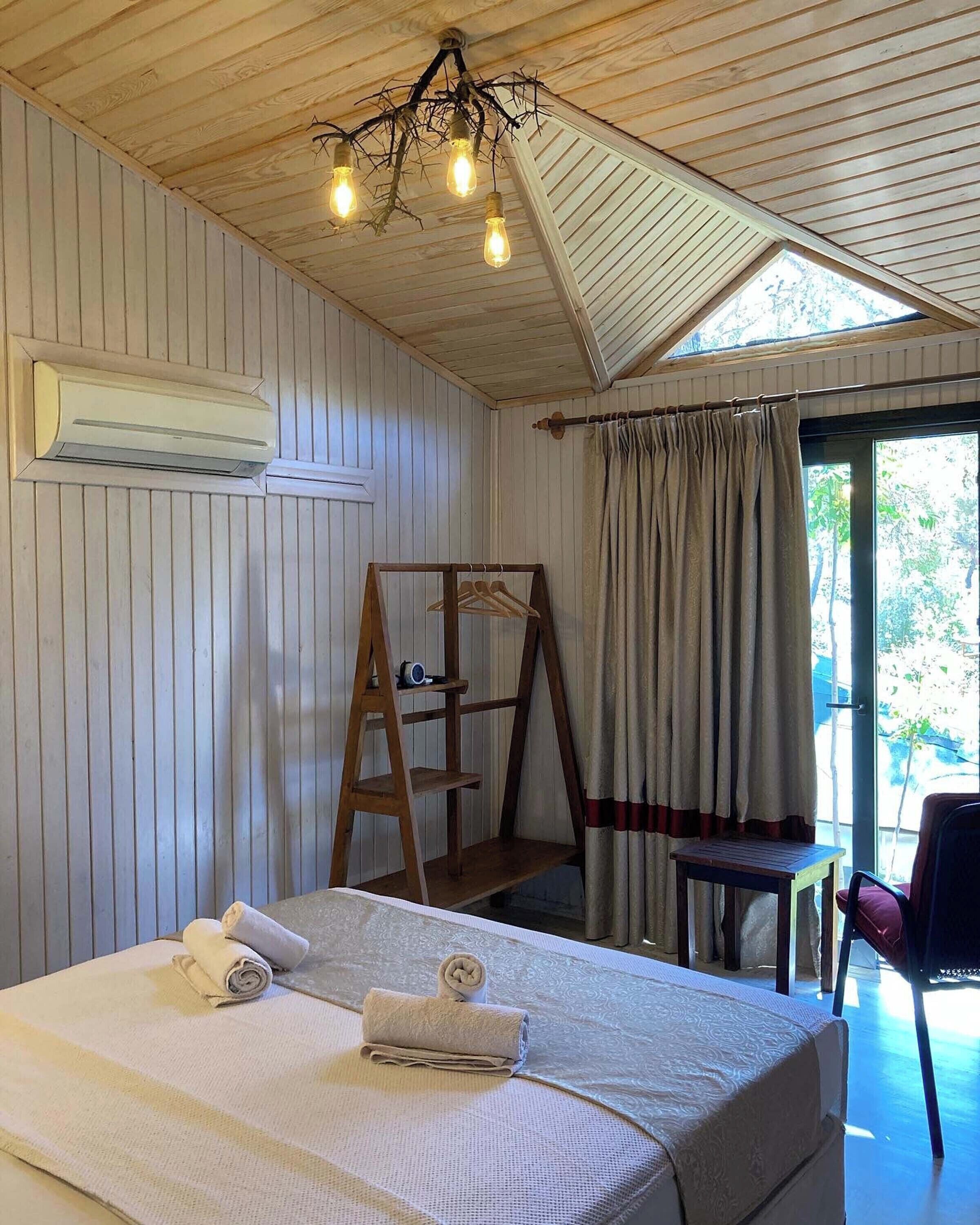 A room with a bed, an air conditioner, a wooden ladder, a table, and a chair.