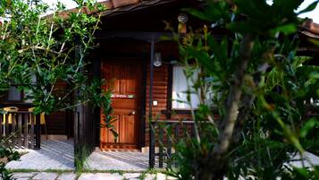 A wooden cabin with a stone-tiled entrance, a wooden door labeled "QUEEN," and a small outdoor seating area with yellow chairs.