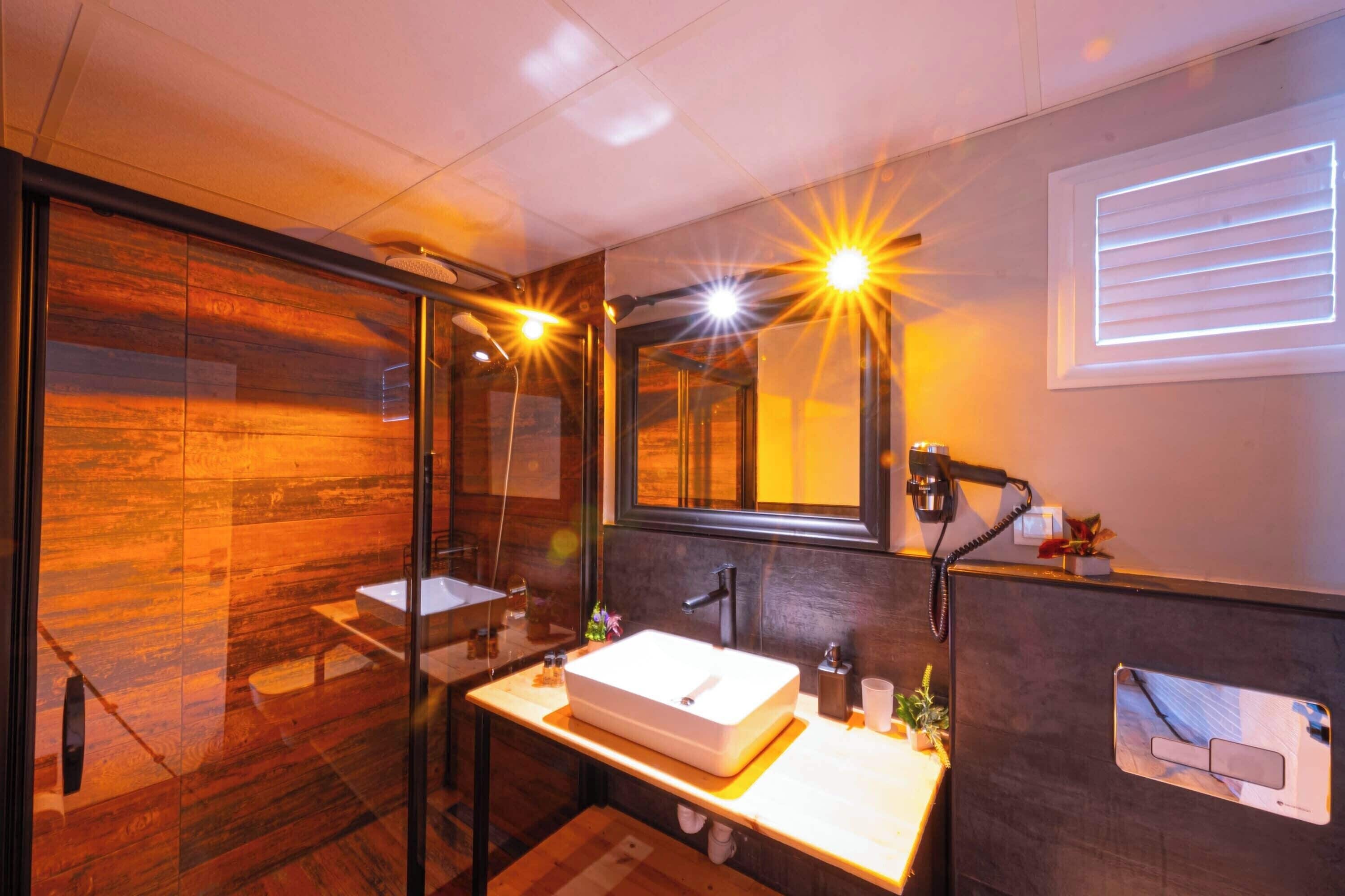 Un baño moderno con cabina de ducha de vidrio, un lavabo blanco e iluminación integrada en el espejo.