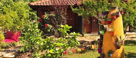 A rustic house with a tiled roof, surrounded by lush greenery and potted plants.