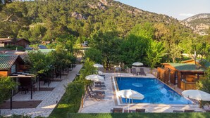 A pool area with lounge chairs and umbrellas, surrounded by greenery and buildings. - Koala Bungalows (Kumluca)