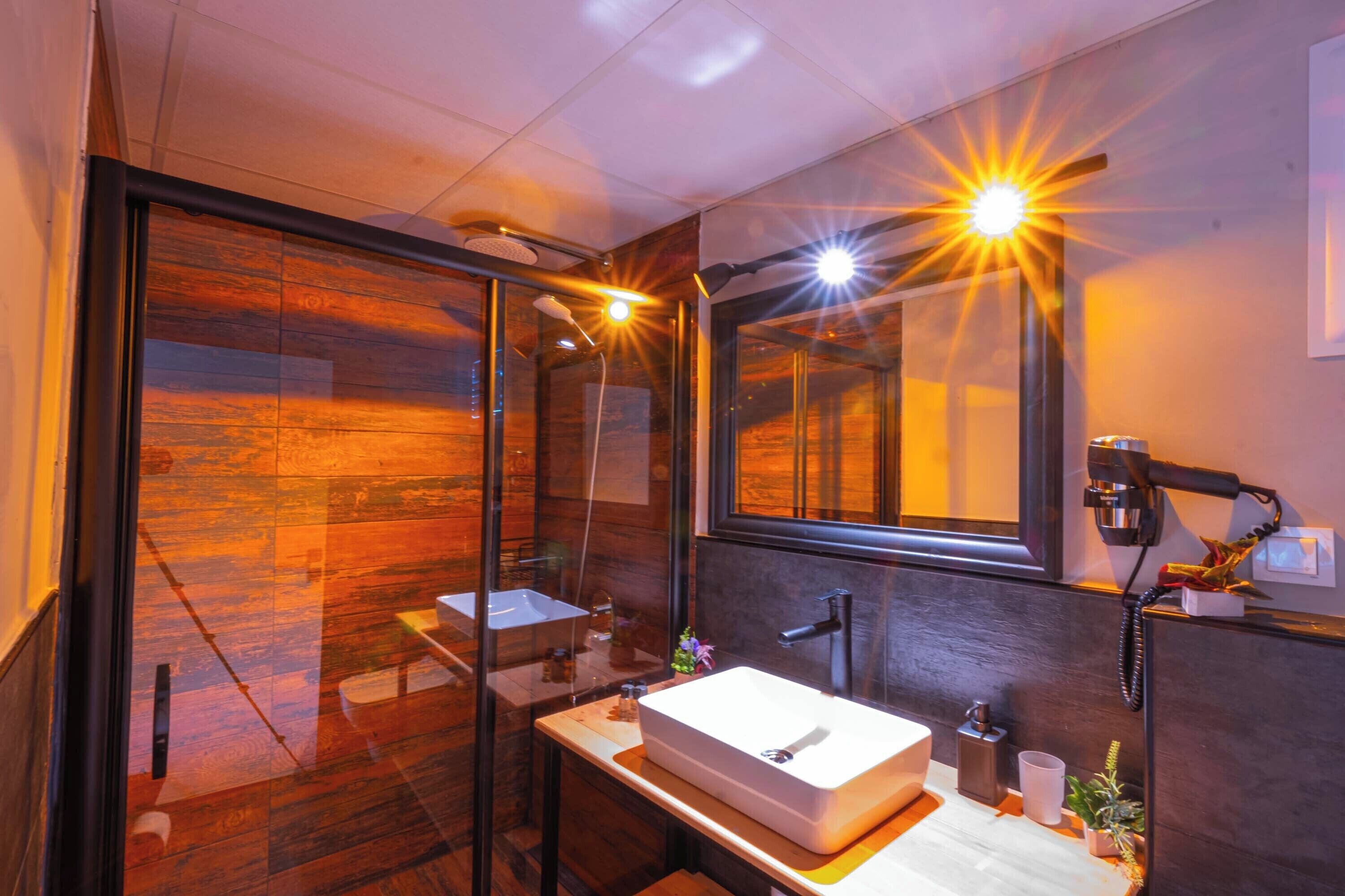 A modern bathroom with a glass shower enclosure, a large mirror, and a wooden floor.
