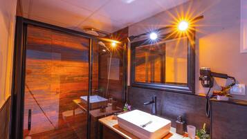 A modern bathroom with a glass shower enclosure, a large mirror, and a wooden floor.