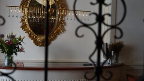 Een kamer met een decoratieve spiegel, een kroonluchter en een bloemenvaas op een houten toonbank.