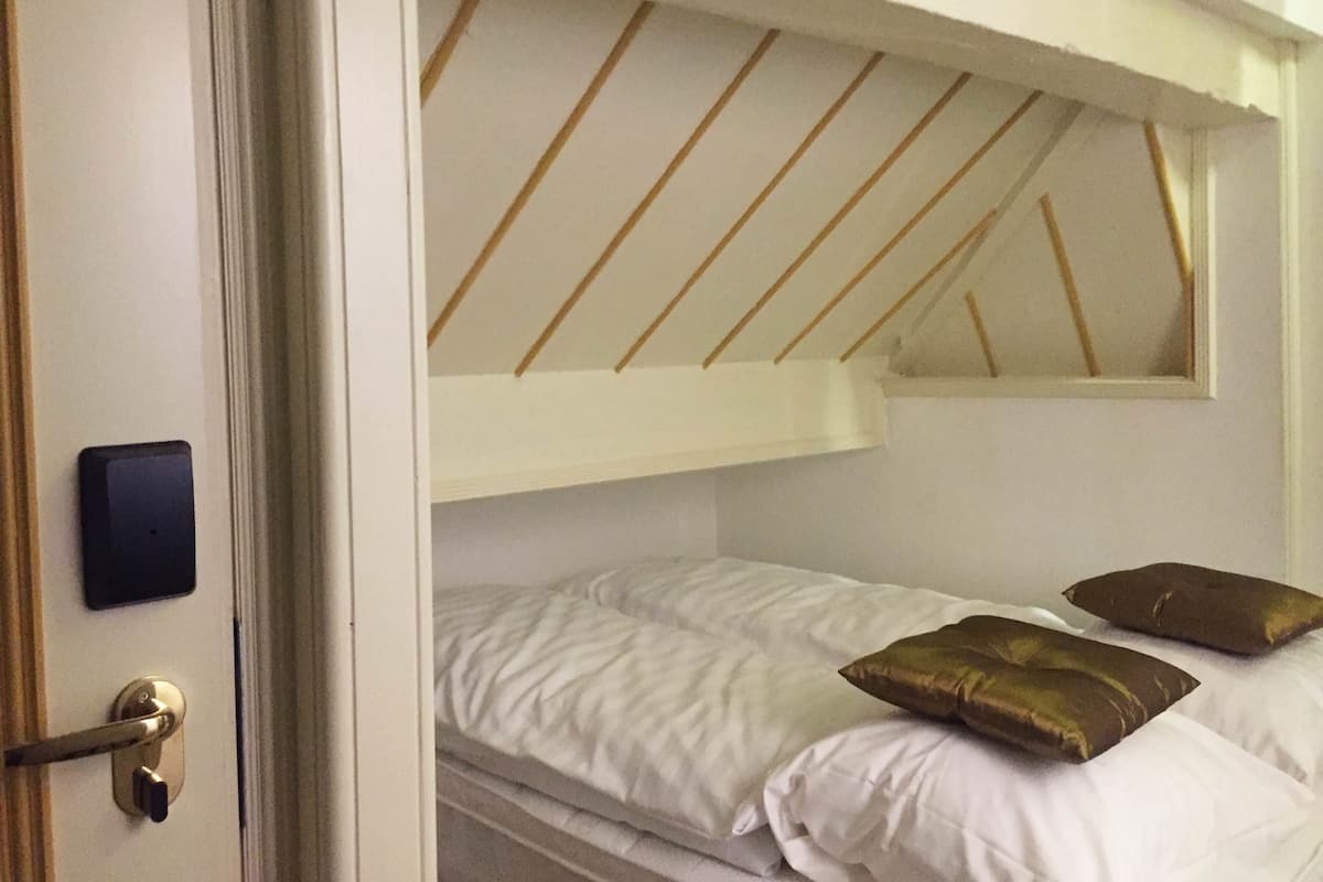 Una habitación con una cama litera, una puerta con cerradura y una pequeña ventana sobre la cama.