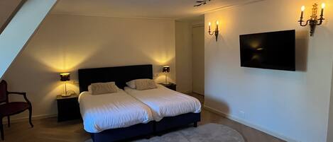 A bedroom with a bed, two bedside tables, a chair, a TV, and a ceiling light fixture.