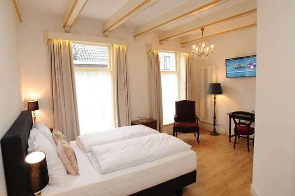 Une chambre d’hôtel avec un grand lit, un bureau, une chaise, une télévision et un lustre.
