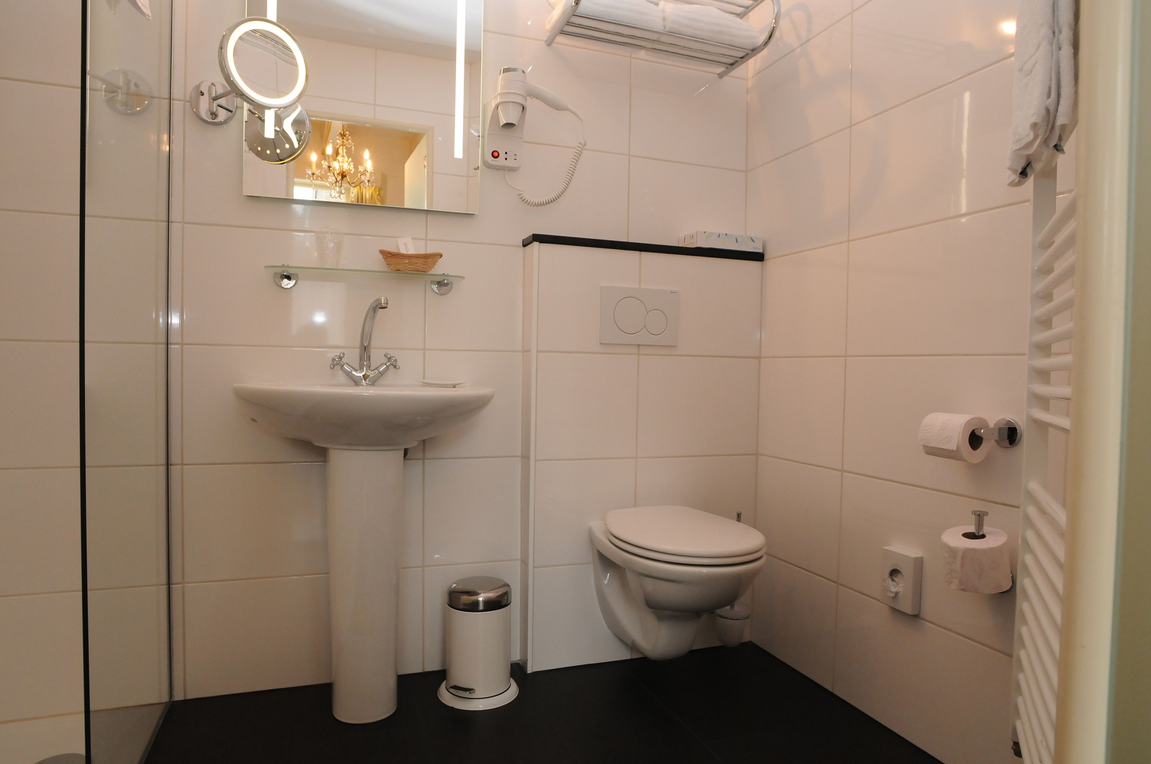 Un baño moderno con lavamanos pedestal, inodoro y espejo con iluminación.
