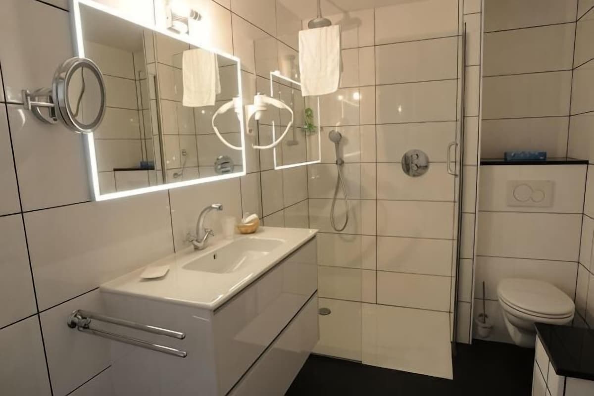 Un baño moderno con lavamanos, espejo y ducha blancos.
