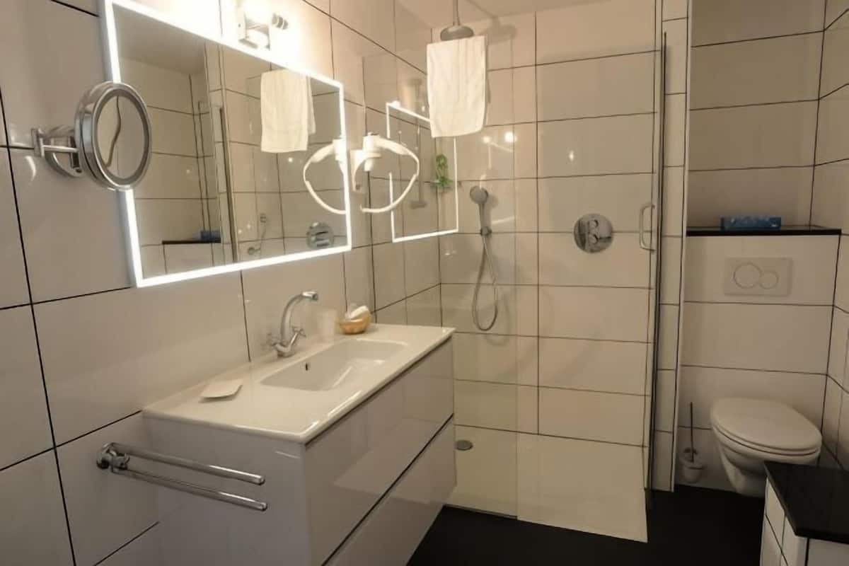 Un baño moderno con lavamanos, espejo y ducha blancos.