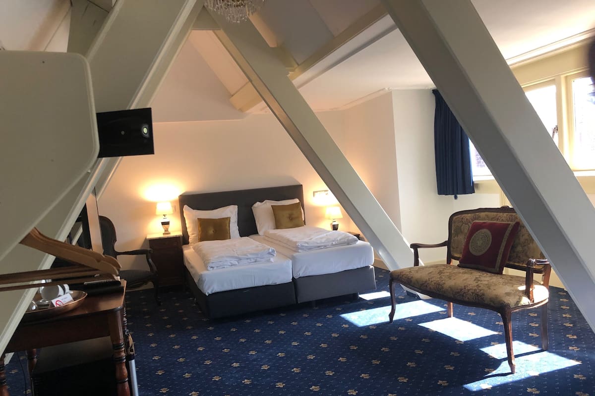 Habitación de hotel con cama, mesitas de noche, una silla y un candelabro.