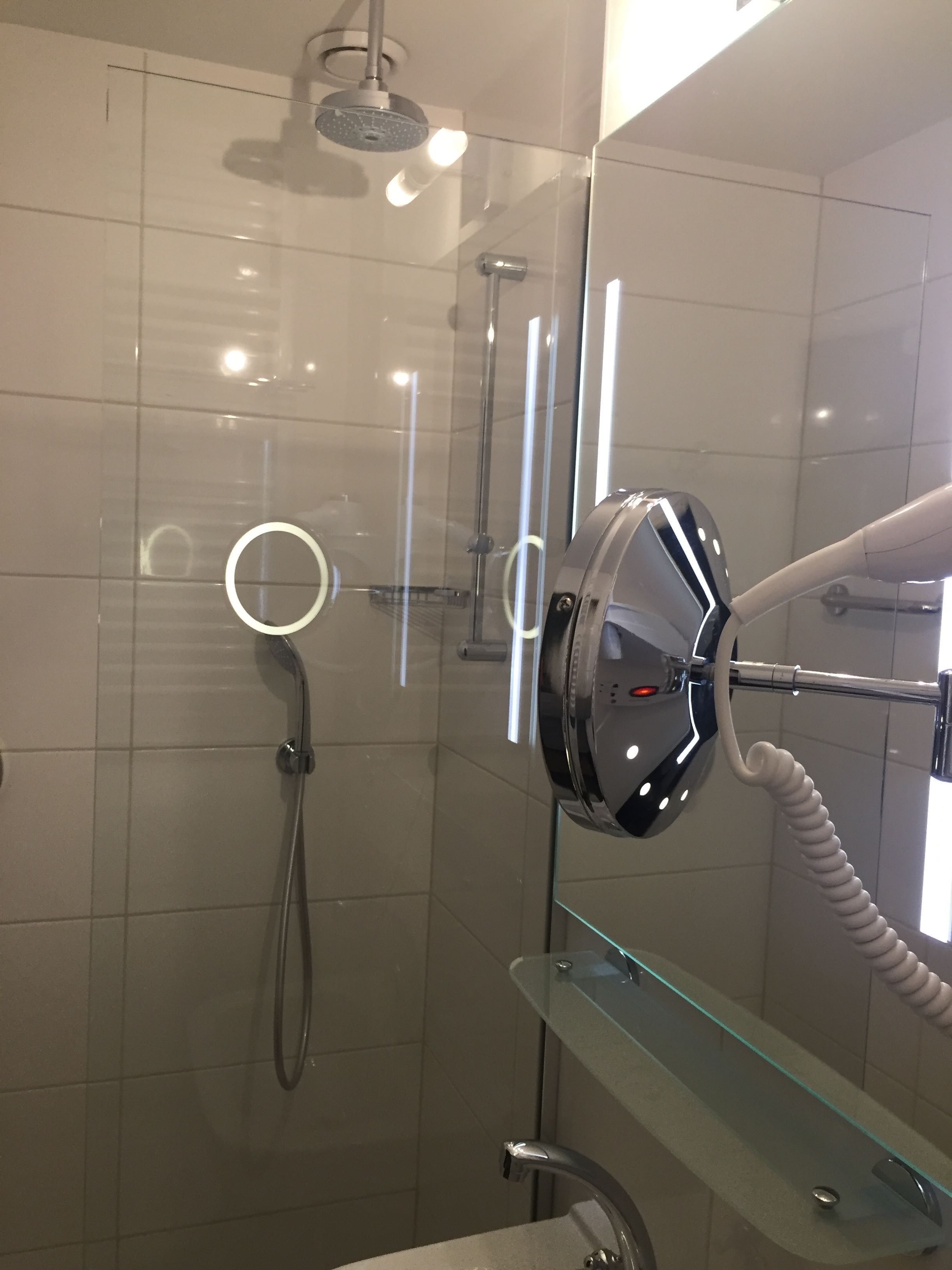 Ein modernes Badezimmer mit einer Duschkabine, einer Handbrause, einem Handtrockner und Ablagefläche aus Glas.