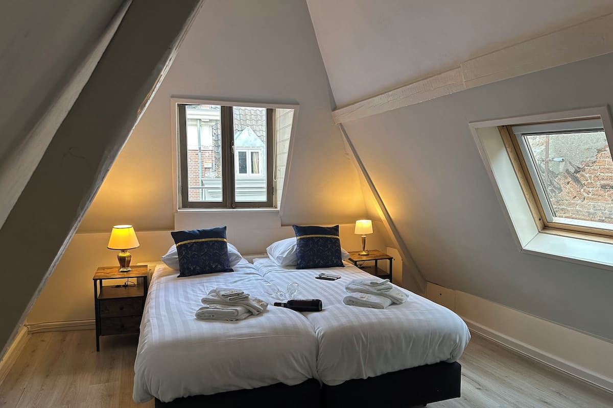 Un dormitorio con una cama grande, dos mesitas de noche con lámparas, una ventana y un tragaluz.
