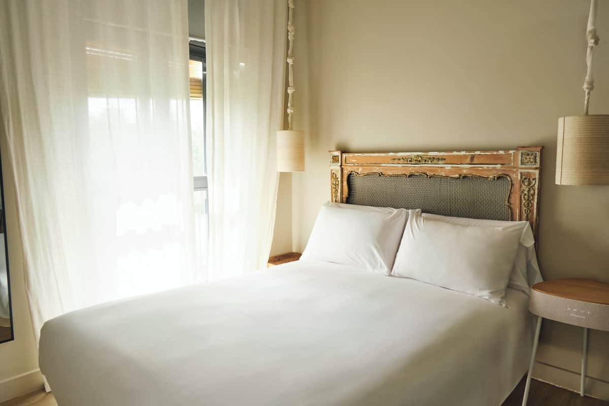 Una cama bien tendida con sábanas blancas, un cabecero de madera con intrincados grabados y una lámpara de noche sobre una mesita.