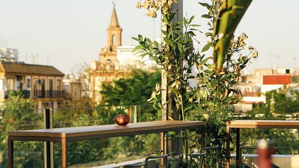 A rooftop terrace with a view of a church spire, metal railings, and a table with chairs. - The Corner House (Seville)