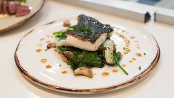 A plate of food with a piece of fish, greens, and mushrooms.