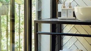 A bathroom with a black shelf holding toiletries and towels, a large mirror, and a window with a view of greenery. - The Corner House (Seville)